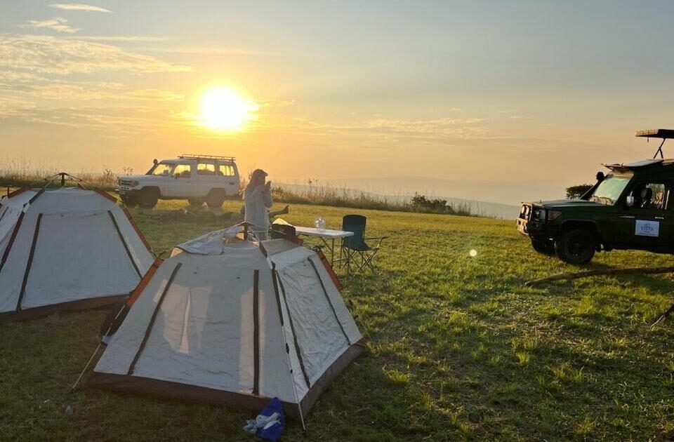 Camping in Akagera National Park with safari tents and vehicles overlooking the Rwandan savannah at sunrise.
