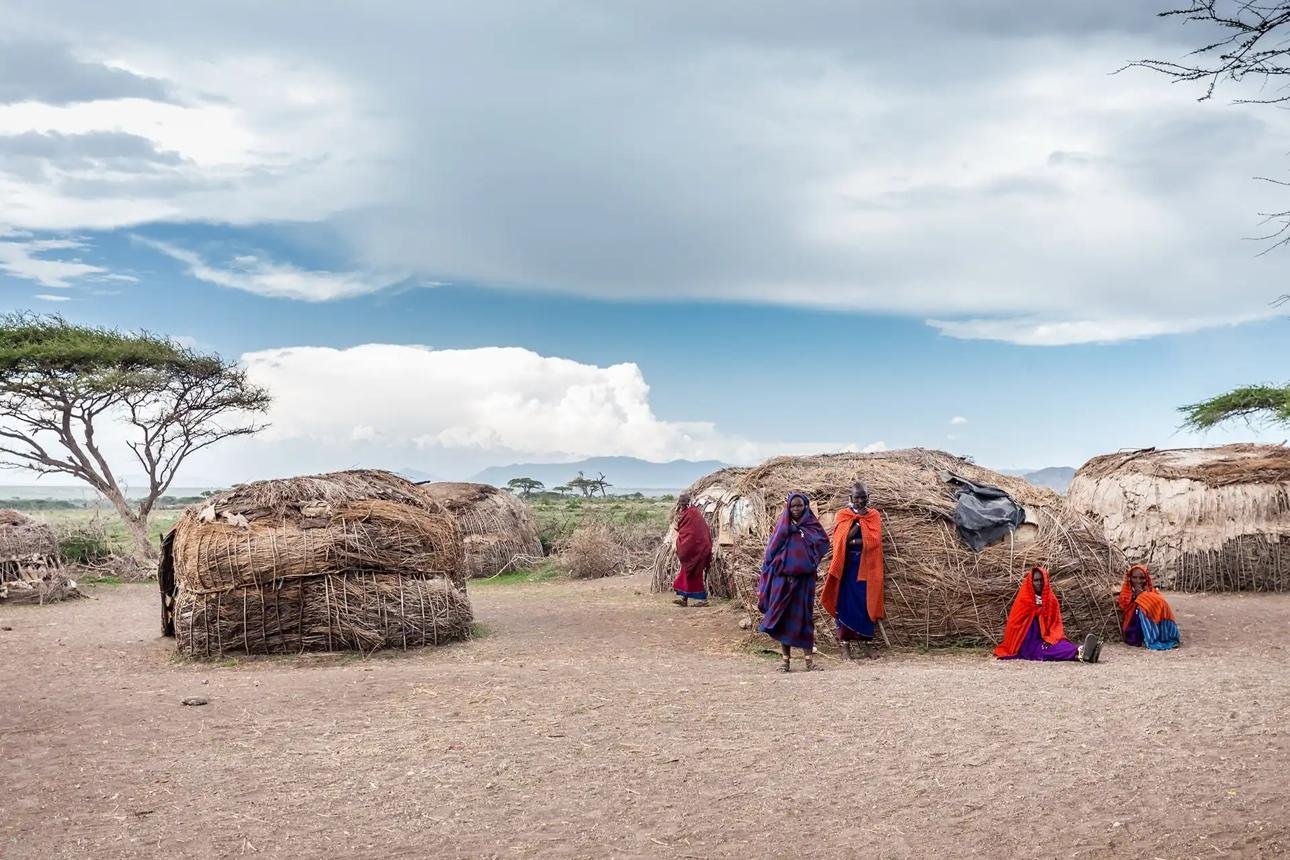 Traditional Maasai homes and community members wearing colourful shukas in a rural East African village.